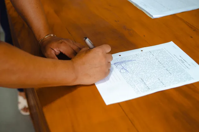 Close-up of hands signing a legal document on a wooden table indoors. Tennessee sealed adoption records in Nashville: disclosure steps and a country music family example
